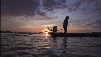 Silhouette of asian fisherman is driving a wooden boat in the river with sunrise morning background . video