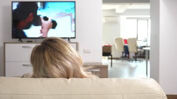 Couple in their cozy flat watching a TV show lying on the couch. Dolly slider back 4K shot video