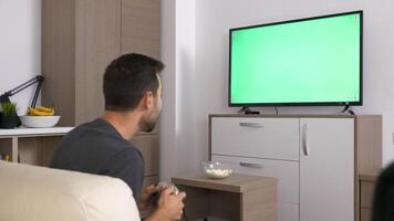 Man playing a video game on the console in front of green mockup screen on big plasma TV. Dolly slider 4K footage