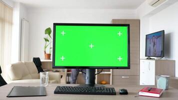 Modern personal computer with big green screen chroma mock up in the living room of comfy house. A man walks in background while the TV is on and sits on the sofa looking at the phone video