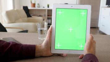 Holding een digitaal tablet pc in verticaal positie met groen scherm chroma bespotten omhoog Bij de tafel in de leven kamer van de huis. dolly schuif 4k beeldmateriaal met parallax effect video