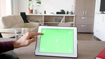 Man touching a digital tablet PC screen with chroma mock up on it. The gadget is on the table in comfy house. video