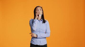 Filipino person savouring cup of coffee in studio, drinking caffeine refreshment for energy through the day. Young woman enjoying hot beverage while standing over orange background. video