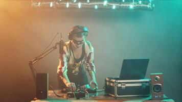 Young artist mixing with turntables on stage, preparing to mash techno and disco music to have fun at nightclub party. DJ performer with crazy makeup using mixer on table. Tripod shot. video