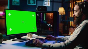 Man talking with friends online while playing together in multiplayer game on green screen desktop PC. Gamer cooperating with teammates in coop videogame using mockup monitor video