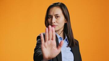 Filipino woman showing stop sign with palm, advertising negativity and no symbol on camera. Female model wearing formal attire in studio, showcasing rejection and refusing something. video