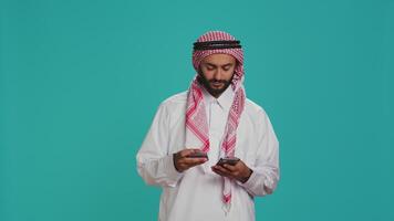 Joyful model using card to make payment while shopping on clothing store website using smartphone app. Middle eastern adult in islamic costume doing banking transfer to buy on sale. video