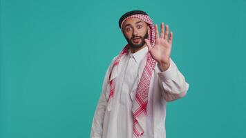 Muslim man showing stop symbol with palm, presenting negativity and disapproval in studio. Young person expressing rejection, being displeased or disagreement over blue background. video