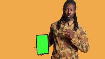 African american guy shows greenscreen on tablet, presenting isolated chromakey display and smiling in front of camera. Young adult holding mobile device with copyspace blank layout. video