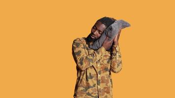 Sleepy adult taking a nap standing over orange background, using pillow to get some sleep in studio. African american person feeling exhausted and napping on camera, falling asleep. video