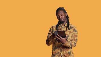 Modern person navigating online on tablet in studio, using mobile device to check social media apps and browse internet pages. African american man checking websites on gadget. video