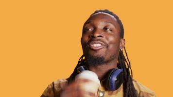 Cheerful guy serving hot cup of coffee in studio, enjoying beverage to gain more energy. African american smiling man drinking caffeine beverage on camera, feeling relaxed and pleased. video