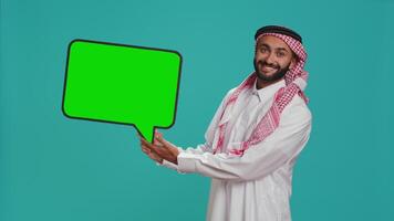 joven adulto participación habla burbuja en cámara, creando web anuncio para nuevo promocional marketing. árabe chico trabajando en comercial eslogan con blanco cartulina icono, cartelera signo. video