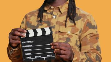 African american film producer using clapperboard for movie industry, identify all takes on filming production. Smiling director holding flap board to cut scenes, yelling action on set. video