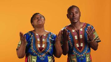 Ethnic couple praying to God with arms spread on camera, showing belief in spirituality and religion. African american people asking for a miracle, begging for good luck and fortune in studio. video