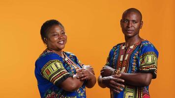 African american couple in traditional attire posing on camera, feeling confident with their lifestyle and culture. Smiling man and woman standing in studio, wearing colorful clothing. video