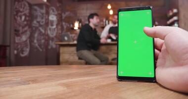 Man swipes on the phone with green screen in a vintage cafe while a customer is talking with the bartender at the counter video