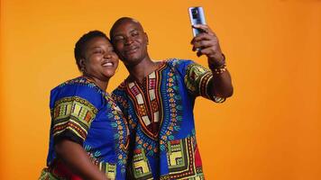 Happy african american couple capturing cute moment in studio, taking pictures on smartphone and enjoying leisure activity. Romantic married people take photos for memories on phone. video