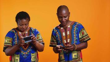 Happy man celebrating videogames win on camera, playing mobile phone gaming contest with his girlfriend. Ethnic woman losing competition while her husband is winning, studio shot. video