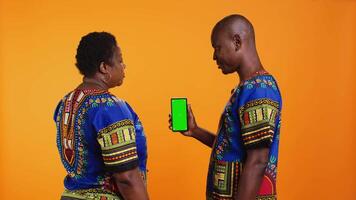 African american couple looking at greenscreen on phone layout, using isolated chromakey template on display. Man and woman pointing at blank copyspace mockup mobile phone screen. video