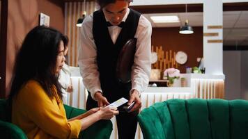 client en utilisant nfc mobile Paiement à acheter café de bar, serveur portion boisson dans salon zone. asiatique voyageur relaxant dans Hôtel lobby, fabrication téléphone Paiement à pos Terminal, hospitalité industrie. video