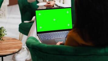 Hotel guest using laptop with greenscreen layout in lobby, looking at copyspace chromakey display in lounge area. Modern person holding pc showing isolated mockup template on screen. video