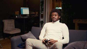 African american man plays intense online videogame, spamming attack buttons on controller. Gamer participating in esports tournament, sitting on couch and playing on gaming console video