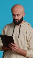 verticale vidéo arabe gars en utilisant tablette à faire défiler sur en ligne sites Internet, à la recherche pour quelque chose sur le l'Internet et en utilisant social médias applications. moderne la personne travail avec écran tactile dispositif dans studio. caméra 1. video