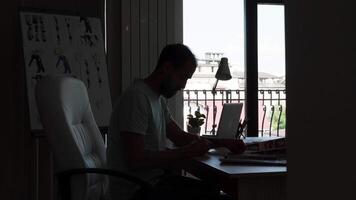 Silhoutte of experienced designer sitting on his desk office while working on computer. Project manager. video