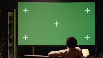 Man using green screen modern TV to watch news program broadcasting in living room. Person watching mockup ultrawide television display showing VOD channel, relaxing on couch video