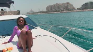 dubai, eua - 5 22 2021. fruta salada deitado em a área coberta do uma privado barco Próximo para uma jovem moreno mulher. uma mulher senta às a arco do a barco dentro uma branco bikini e uma luz transparente capa e come fruta video