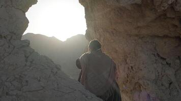 A young bearded shaman prays while standing in a grotto of a rock among the sand dunes of the desert video