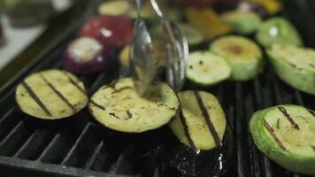 The chef turns over the vegetables that are fried on the grill with metal tongs video