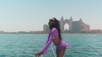 Young swarthy woman in a white bikini and a light dress on board a private boat against the backdrop of the city video