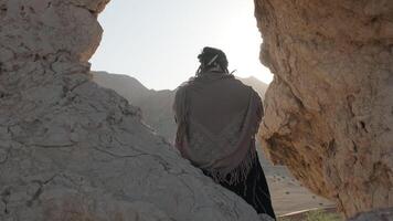 een jong gebaard sjamaan bidt terwijl staand in een grot van een rots tussen de zand duinen van de woestijn video