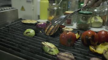 The chef transfers the roasted vegetables from the grill to a large container with metal tongs video