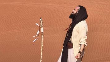 Dubai, VAE - - 1 14 2023. jung bärtig Mann gekleidet wie ein Schamane Tanzen auf Wüste Sand video