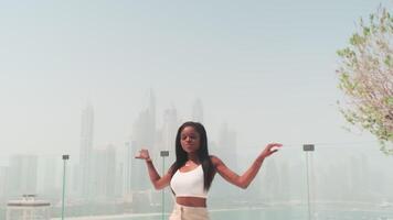 Swarthy young woman in a business white trouser suit on a glass balcony overlooking Dubai, UAE. video