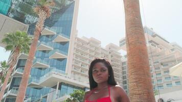 Dubai, UAE - 5 22 2021. Young swarthy woman in a red bikini and a light dress walking barefoot in a private pool video