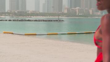 A young swarthy woman in a bikini and a light red dress walks barefoot on a sandy beach in the surf water video