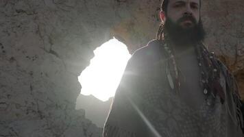 A young bearded shaman prays while standing in a grotto of a rock among the sand dunes of the desert video