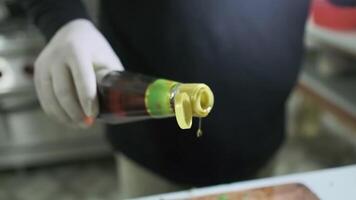 uma luva branca chefe de cozinha derrama óleo a partir de uma garrafa sobre picado e misturado legumes em uma corte borda video