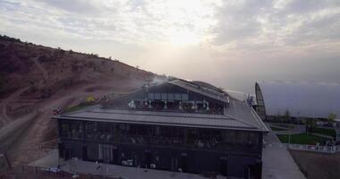 The drone flies around the mountain station of the cable car with a restaurant next to it. Against the background of the sunset sky video