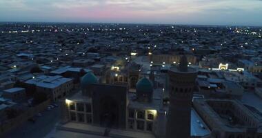 A drone flies over the architectural complex Poi-Kalon among old houses in Bukhara, Uzbekistan. Cloudy night video