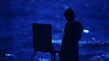 silhouet van een artiest met een ezel tegen de achtergrond van een avond rivier. video