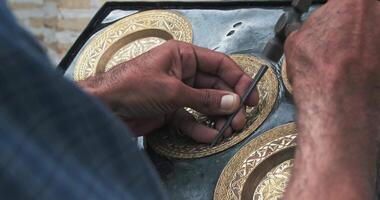 A master embosser creates a pattern on a copper plate using ancient technologies. video