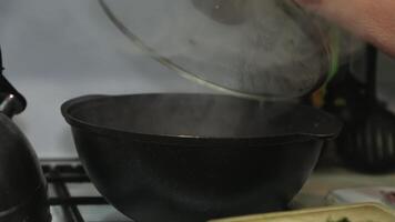 A woman's hand opens the lid of a cauldron with food standing on a gas stove. video