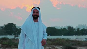 A young bearded businessman in national Arab clothes dances against the background of the sunset. video