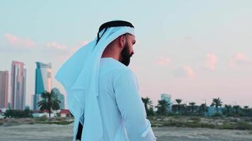 A young bearded businessman in national Arab clothes stands in front of the skyscrapers of Dubai. video