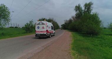 das Drohne fliegt Über ein klein Land Straße umgeben durch Bäume. ein Krankenwagen geht vorbei durch auf das Straße. video